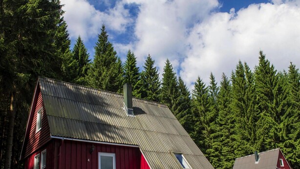 A red wooden cabin with a sloped roof, a chimney, and a small porch. - Holiday Complex Erzgebirge Idyll, Breitenbrunn (Breitenbrunn/Erzgeb.)