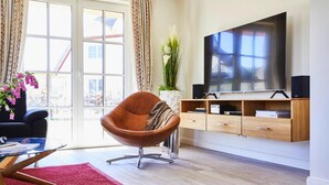 A modern living room with a large flat-screen TV, a brown leather chair, a glass coffee table, and a red rug. - Ferienhaus, Fuhlendorf (Fuhlendorf)