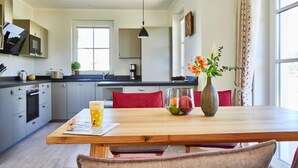 A modern kitchen with grey cabinets, a wooden dining table, and a vase with flowers. - Ferienhaus, Fuhlendorf (Fuhlendorf)