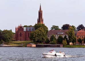 A boat on a river with a church and residential buildings in the background. - Ferienwohnungen, Malchow (Malchow)