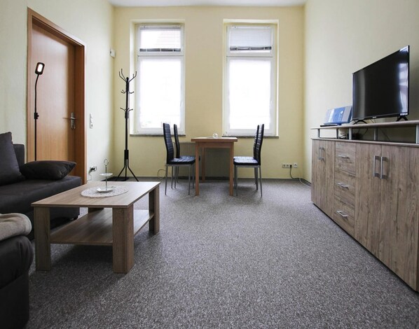 A compact living room with a sofa, a coffee table, a TV on a stand, and a dining table with chairs. - Ferienwohnungen, Malchow (Malchow)