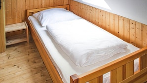 Una cama litera de madera con ropa de cama blanca en una habitación con paredes de madera y techo inclinado.
