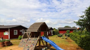 Un terrain de jeux avec un toboggan et un mur d’escalade, situé devant un bâtiment rouge.