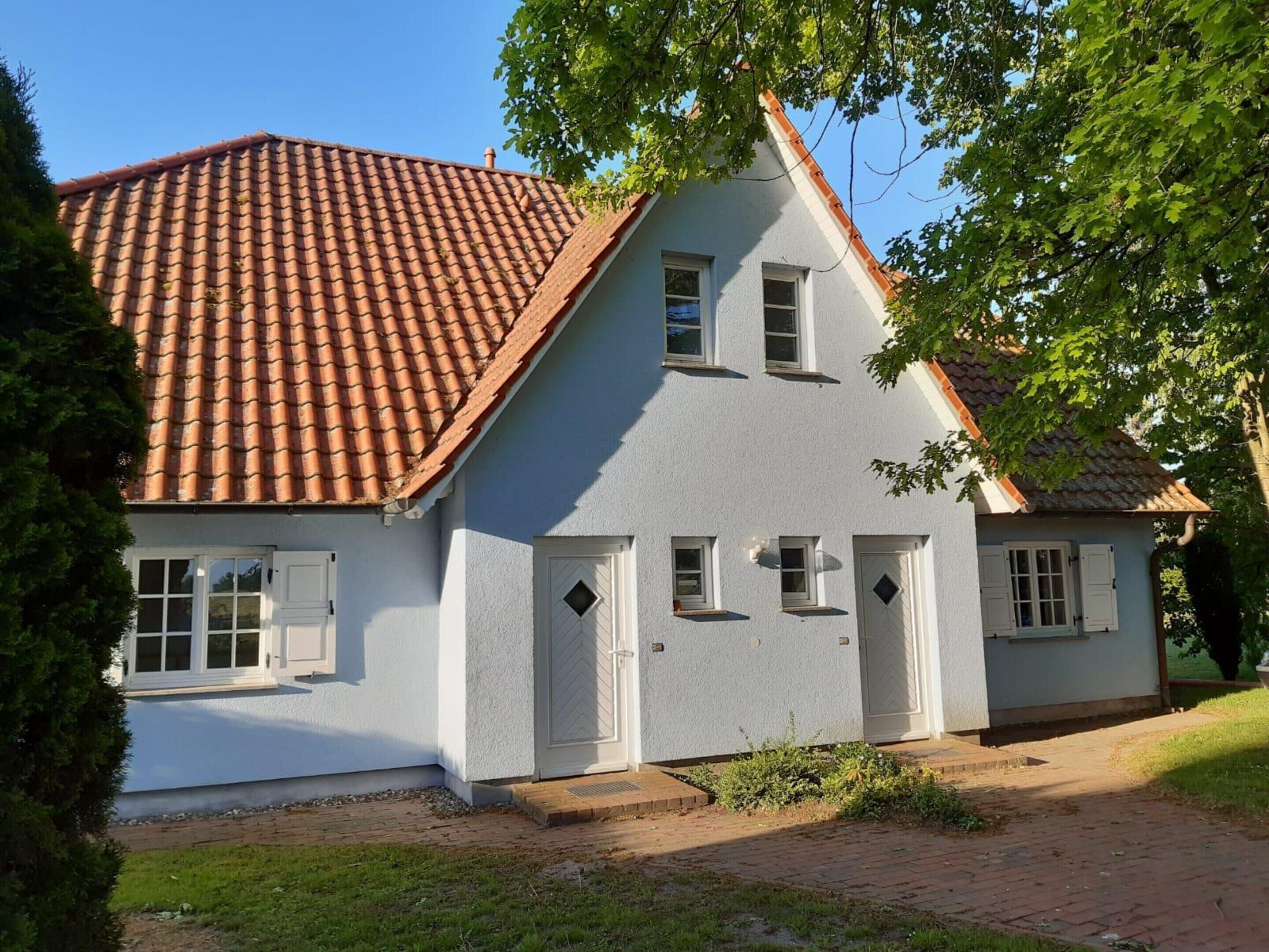 A two-story house with a red-tiled roof, white exterior walls, and a small front porch.