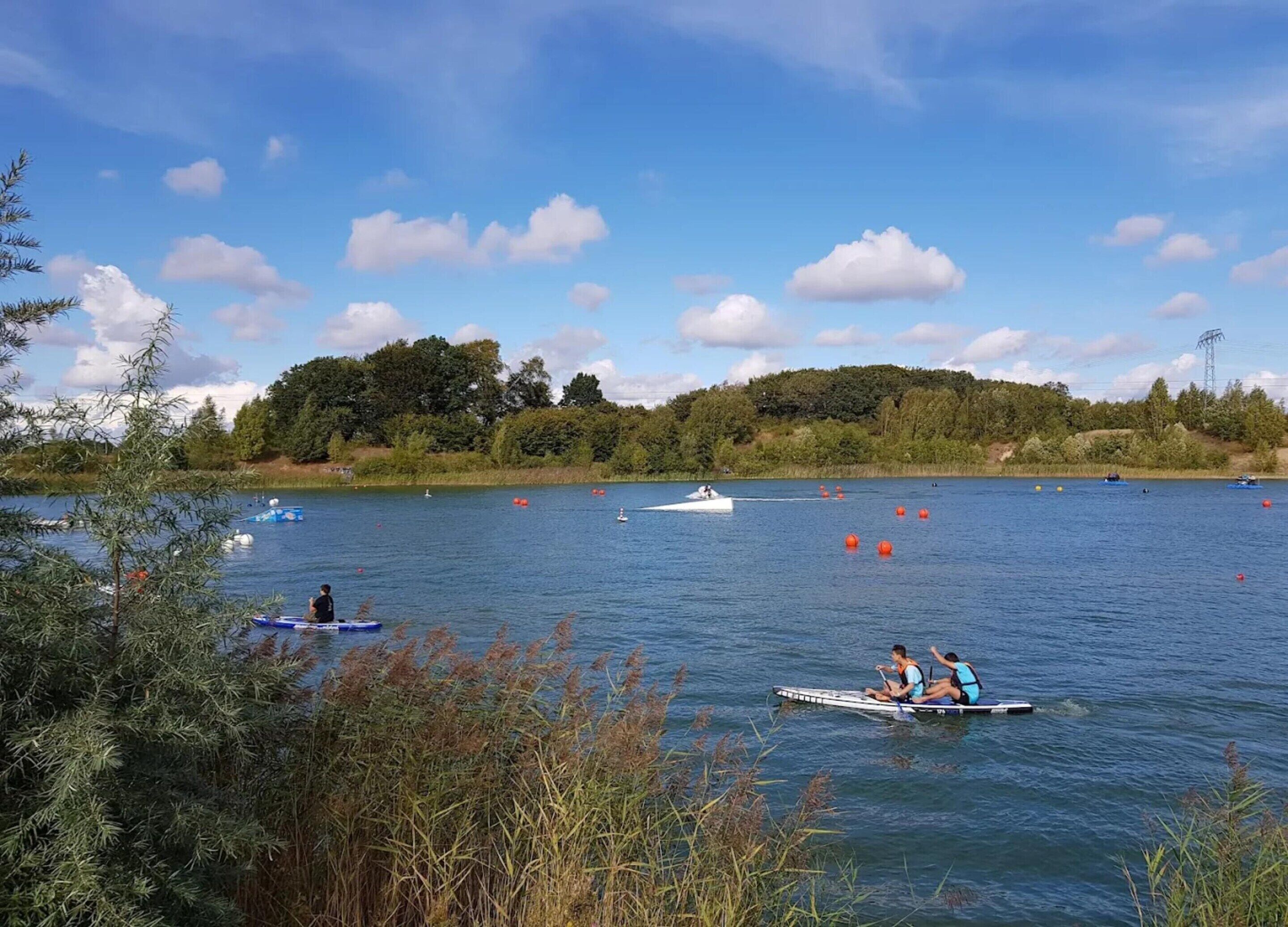 A calm lake with boats and people on the water, surrounded by trees and a clear sky.
