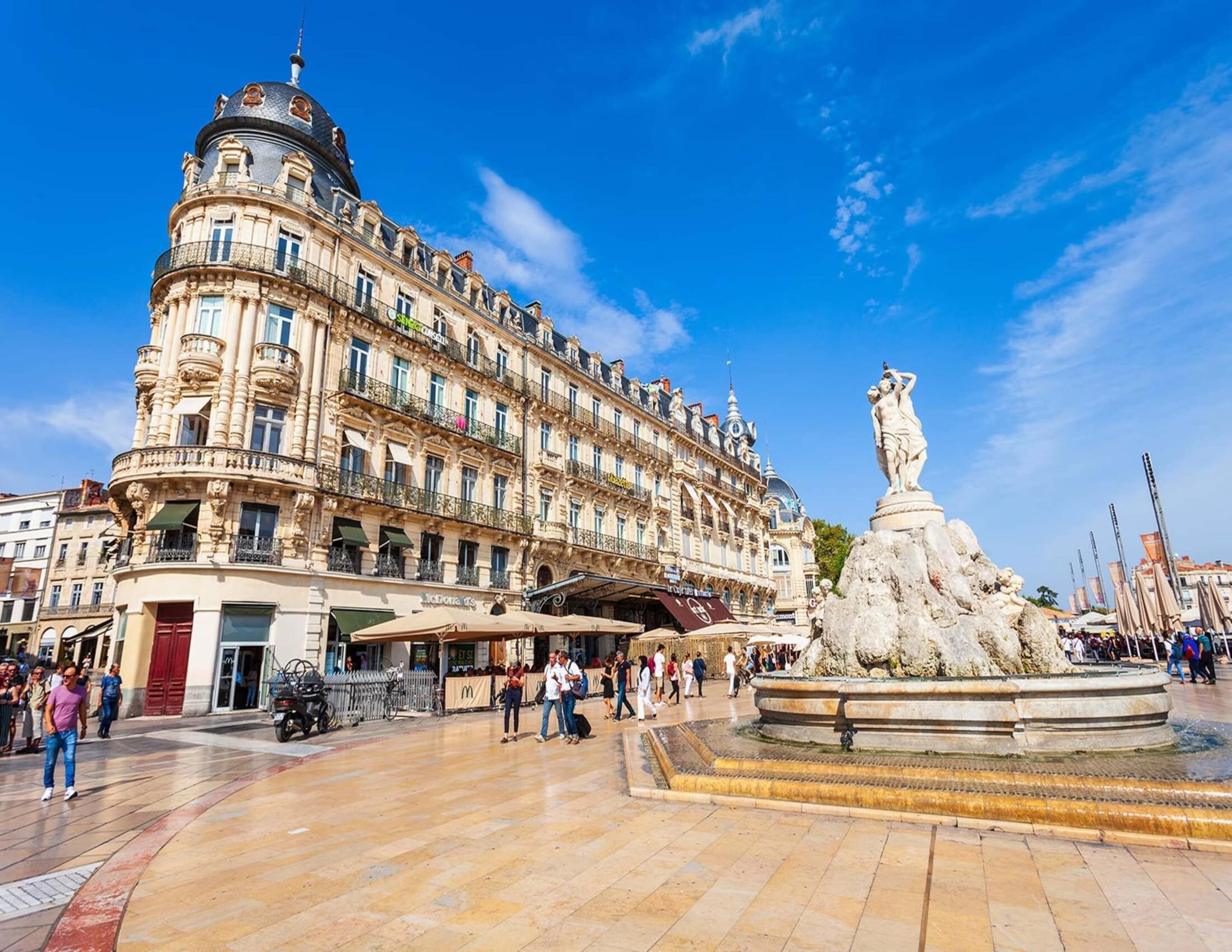 Um edifício histórico com arquitetura ornamentada, uma fonte e uma estátua em primeiro plano.