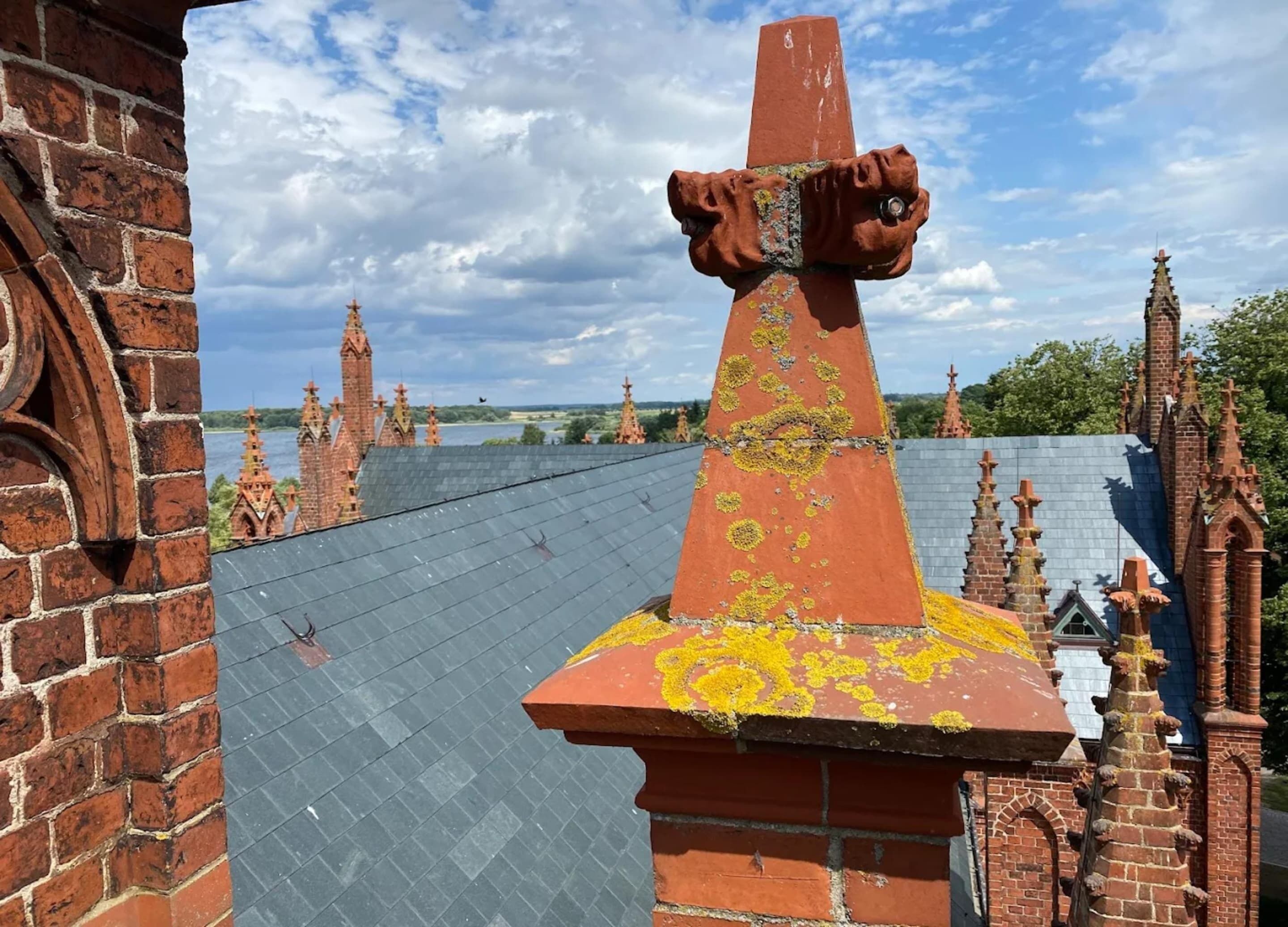 A brick chimney with a unique cross-shaped top, surrounded by Gothic-style architecture.