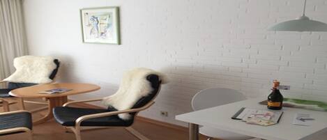 A modern room with a white brick wall, a round table, two chairs, a small white table with a bottle, and a framed picture.