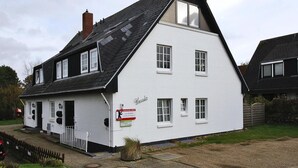 A white building with a black roof, multiple windows, and a sign that reads 'Ursula.' - Ferienwohnung in Westerland auf Sylt (Sylt)