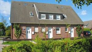 Een tweelaags bakstenen huis met schuin dak, meerdere ramen en een kleine garage.