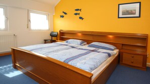 A bedroom with a wooden bed, a nightstand, a chair, and a wall with fish decorations. - Reihenhaus, Dornumersiel (Dornum)