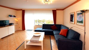Een woonkamer met een bank, een salontafel, een televisie en een raam met gordijnen.