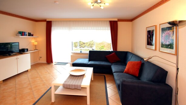A living room with a sofa, a coffee table, a television, and a window with curtains. - Reihenhaus, Dornumersiel (Dornum)