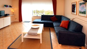 Een woonkamer met een bank, een salontafel, een televisie en een raam met gordijnen.