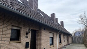 A brick building with a tiled roof, multiple windows, and a visible chimney. - Gemuetliches Reihenhaus mit Garten (Dornum)