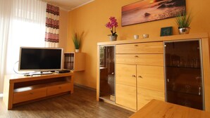 A living room with a wooden cabinet, a television, and a painting of a sunset. - Gemuetliches Reihenhaus mit Garten (Dornum)