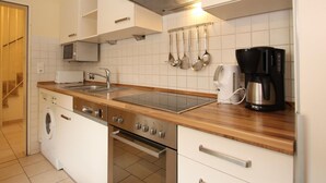A modern kitchen with white cabinets, a stainless steel range, a built-in microwave, a coffee maker, and a dishwasher. - Gemuetliches Reihenhaus mit Garten (Dornum)