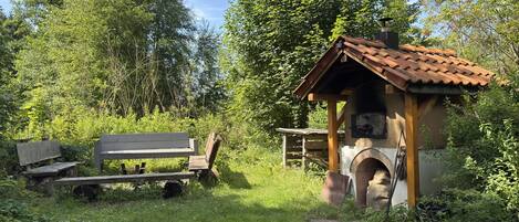 A rustic outdoor seating area with a wooden bench and a small wooden structure with a tiled roof, surrounded by lush greenery.