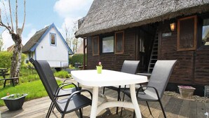 A wooden cabin with a thatched roof, a white table with four chairs, and a small garden area. - Bootshaus in Teterow - Formerly TUI (Teterow)