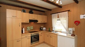 A compact kitchen with wooden cabinets, a built-in oven, a sink, and a window with curtains. - Bootshaus in Teterow - Formerly TUI (Teterow)