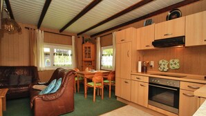A compact living space with a brown leather sofa, a dining table with chairs, a kitchenette with a stove, and a window with curtains. - Bootshaus in Teterow - Formerly TUI (Teterow)