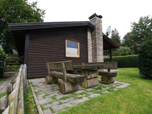 A cabin with a stone chimney, a window, and a picnic table.