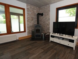 A room with a stone wall, a wood-burning stove, a TV on a white stand, and a window with blinds.