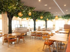 Un restaurante con mesas y sillas redondas, plantas de interior y luces colgantes.