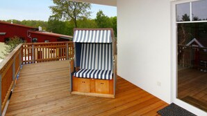 Una terraza de madera con una silla de playa a rayas y un ventanal que da a una zona cubierta.