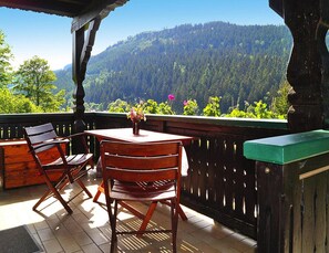 Um deck de madeira com mesa e cadeiras, com vista para uma montanha arborizada.