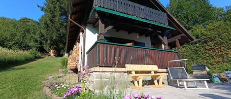 A wooden chalet with a balcony, surrounded by a garden with purple flowers.