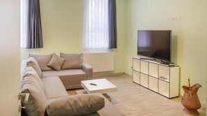 A modern living room with a sofa, a coffee table, a TV on a cabinet, and a radiator. - Ferienwohnung Fachwerktraum, Wernigerode (Wernigerode)