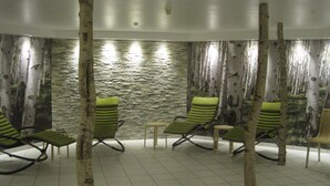 A spa area with four green lounge chairs, a small table, and a stone wall backdrop. - Appartementhaus Jann-berghaus, Norderney (Norderney)