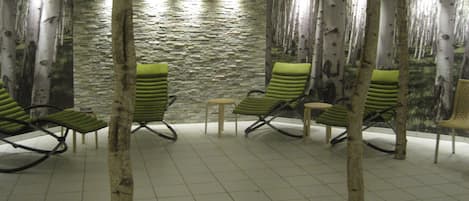 A spa area with four green lounge chairs, a small table, and a stone wall backdrop.