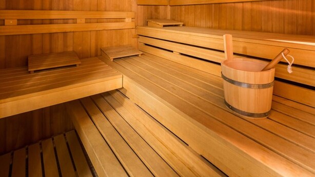 A wooden sauna with benches and a wooden bucket. - Appartementhaus Jann-berghaus, Norderney (Norderney)