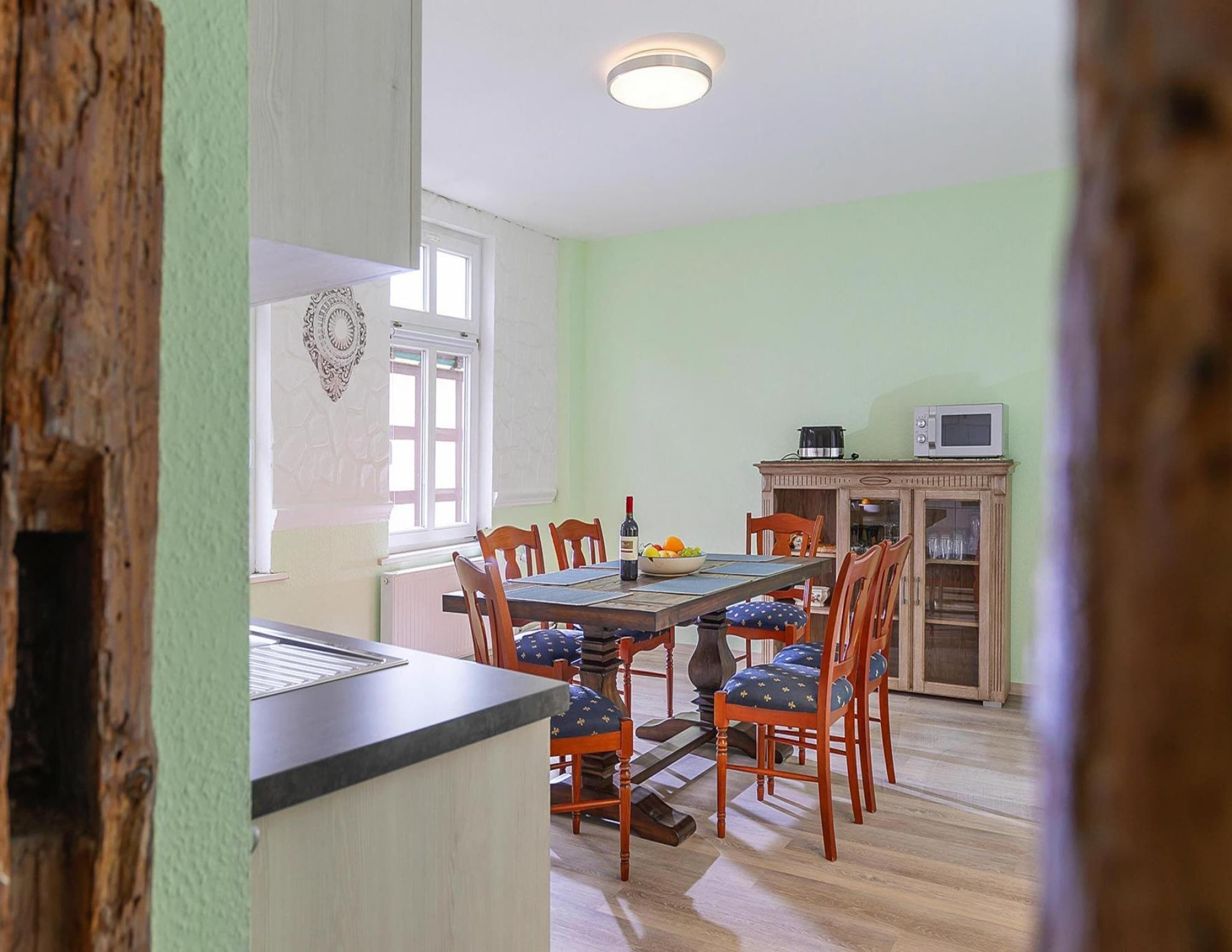 A dining area with a wooden table, chairs, and a microwave on a cabinet.