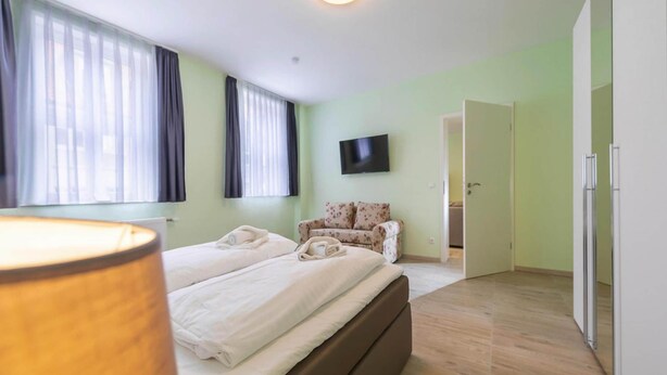 Ein Hotelzimmer mit einem Bett, einem Sofa, einem Fernseher und einer Tür zu einem weiteren Raum.