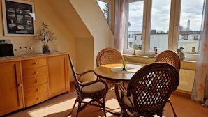 A dining area with a round table, wicker chairs, a wooden cabinet, and a poster on the wall. - Ferienwohnung, Gromitz (Groemitz)
