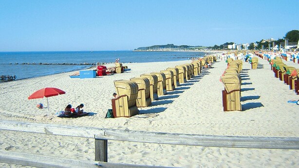 A beach with rows of beach chairs and umbrellas, a sandy shore, and a clear blue sky. - Ferienwohnung, Gromitz (Groemitz)