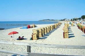 A beach with rows of beach chairs and umbrellas, a sandy shore, and a clear blue sky. - Ferienwohnung, Gromitz (Groemitz)