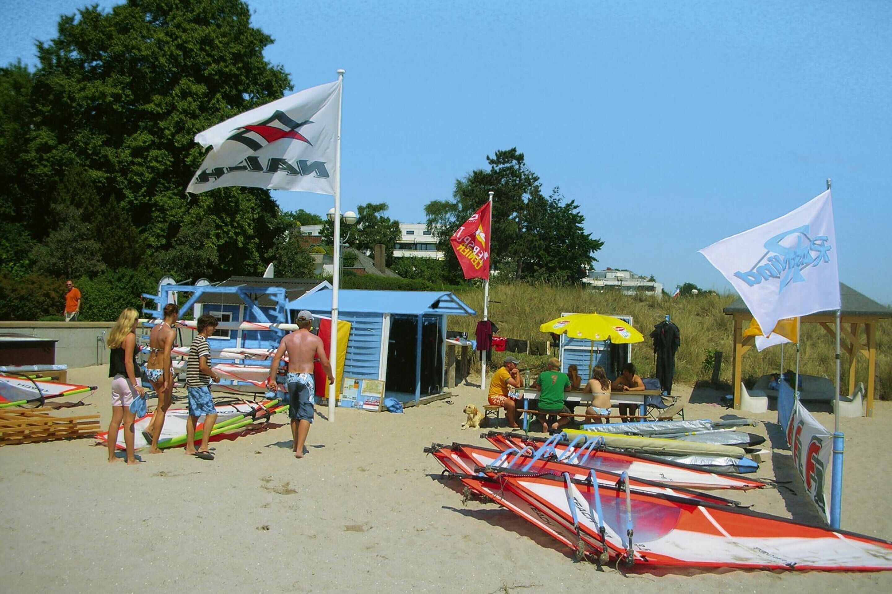 A beach with beachgoers, a small hut, and several kites.