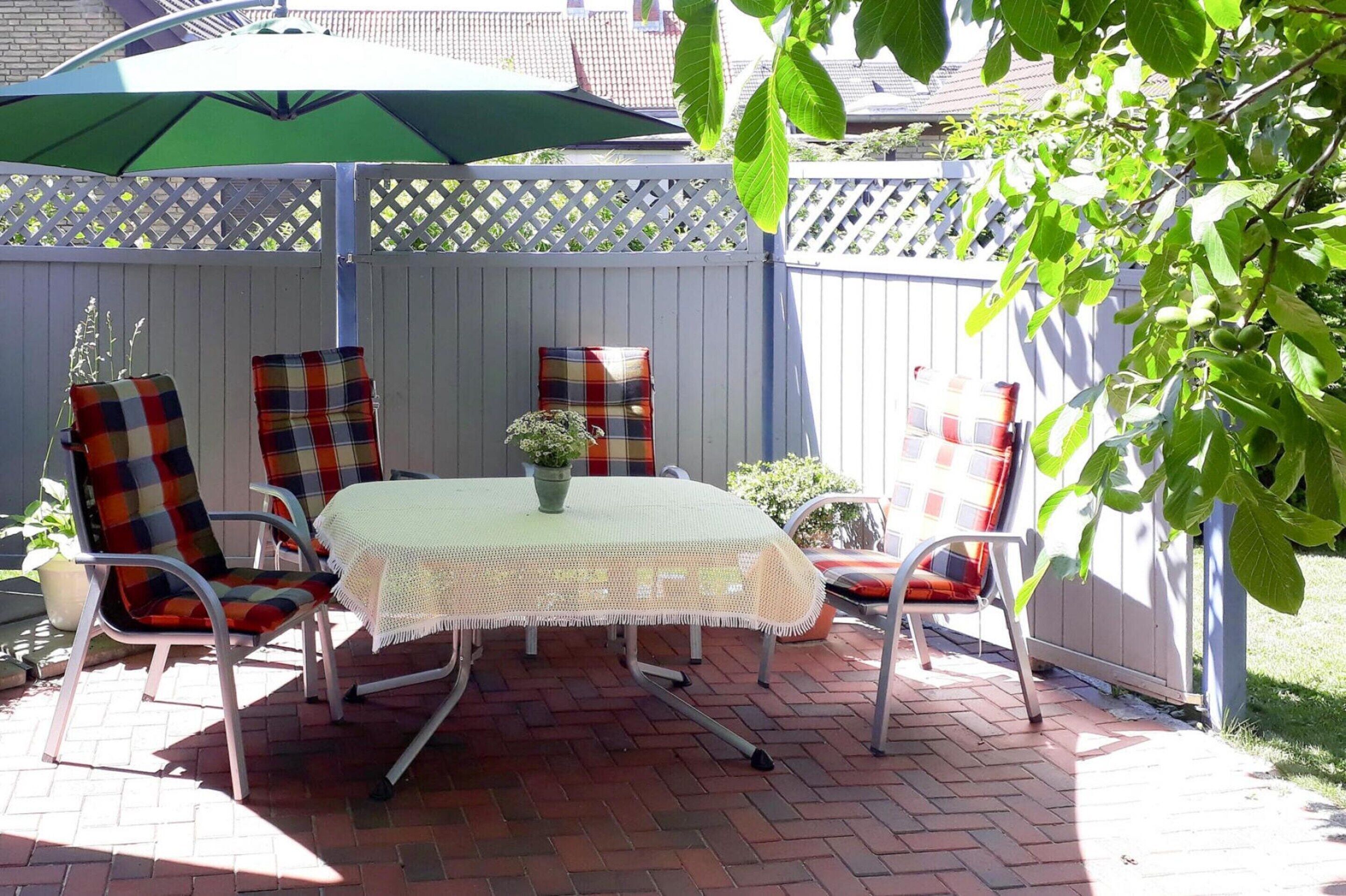 A patio with a table and four chairs, a green umbrella, and a white fence.