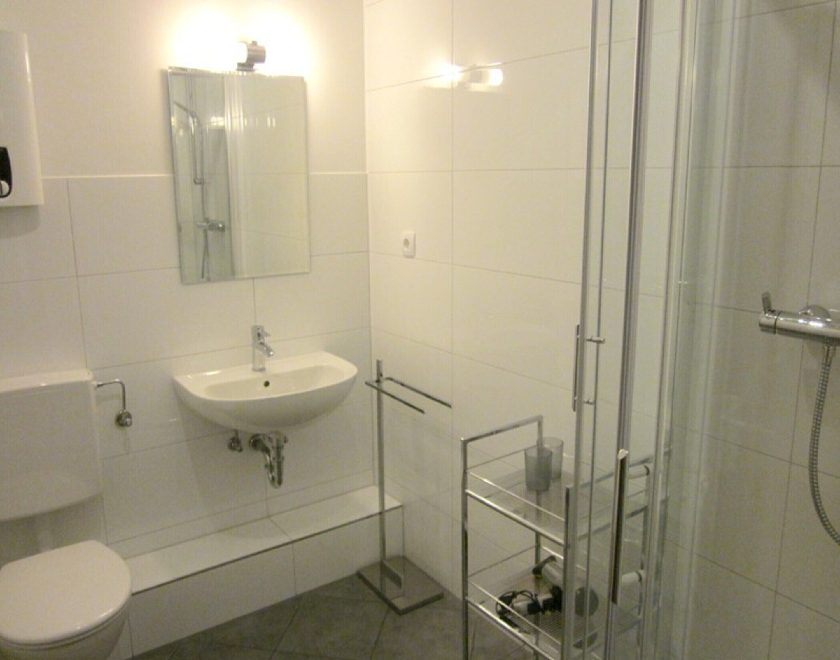 Ein modernes Badezimmer mit einem weißen Waschbecken, einem Spiegel, einer Duschkabine aus Glas und einer Toilette.