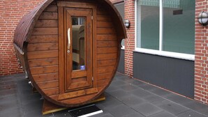 A wooden barrel-shaped structure with a door, positioned on a paved surface next to a brick building with a window. - Ferienwohnung in Westerland auf Sylt (Sylt)