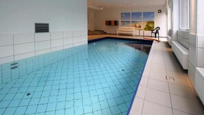 An indoor swimming pool with tiled walls and floor, a bench, and a window with blinds. - Ferienwohnung in Westerland auf Sylt (Sylt)