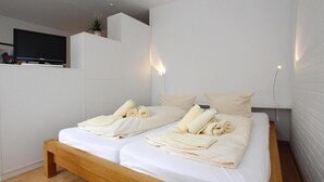 A modern bedroom with a wooden bed, white linens, and a flat-screen TV on a white wall. - Ferienwohnung in Westerland auf Sylt (Sylt)