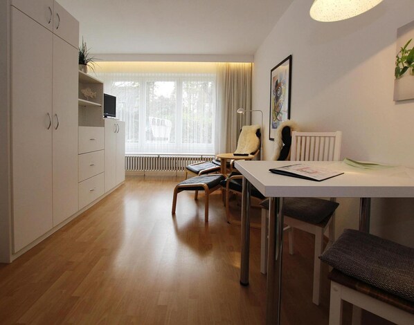 A modern, well-lit room with a dining table, chairs, a sofa, and a TV.