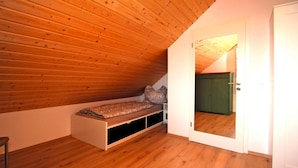 A small bedroom with a sloped ceiling, a single bed, a green wardrobe, and a door leading to another room.
