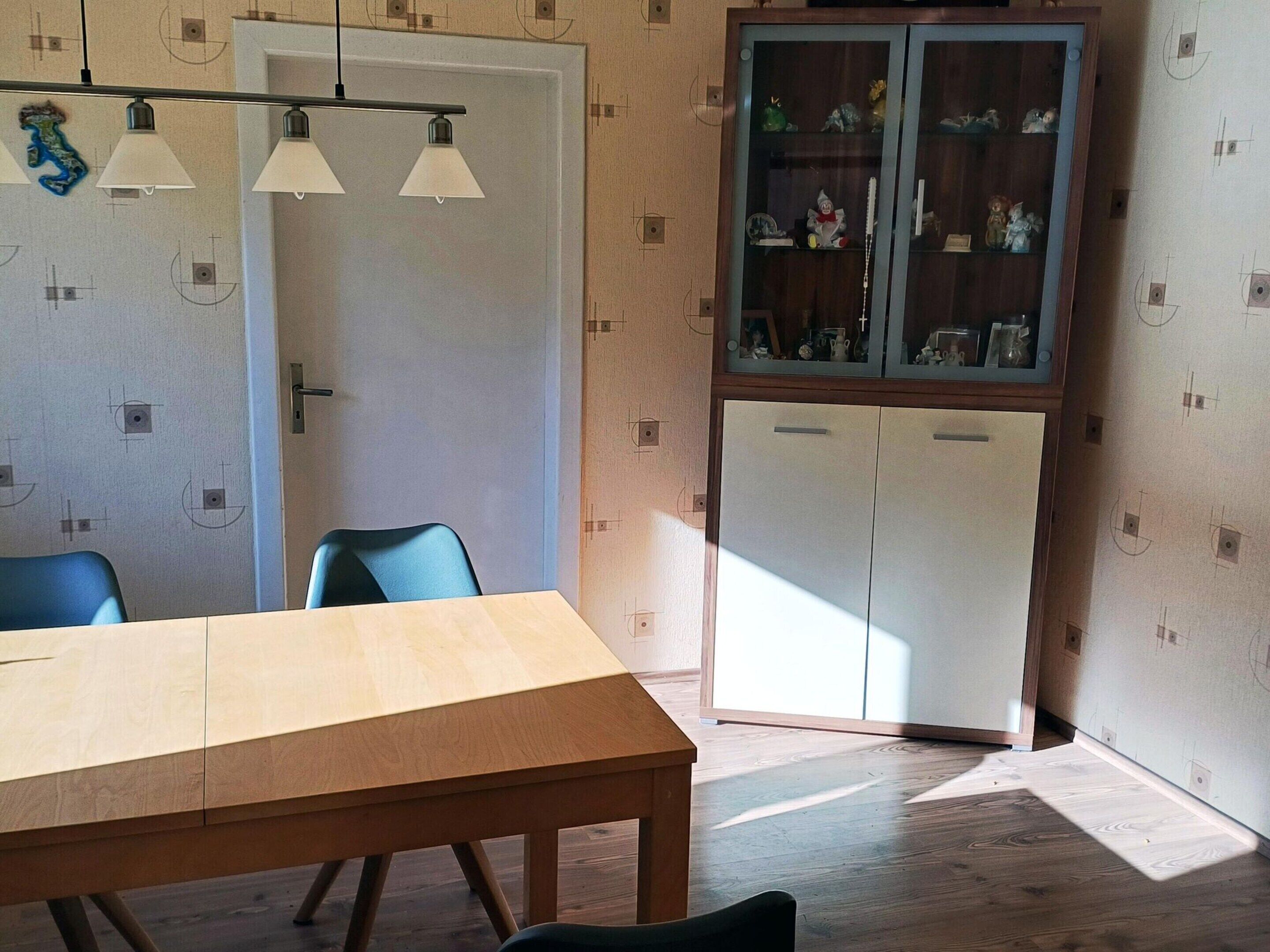 A dining area with a wooden table and chairs, a cabinet with glass doors, and a ceiling light fixture.