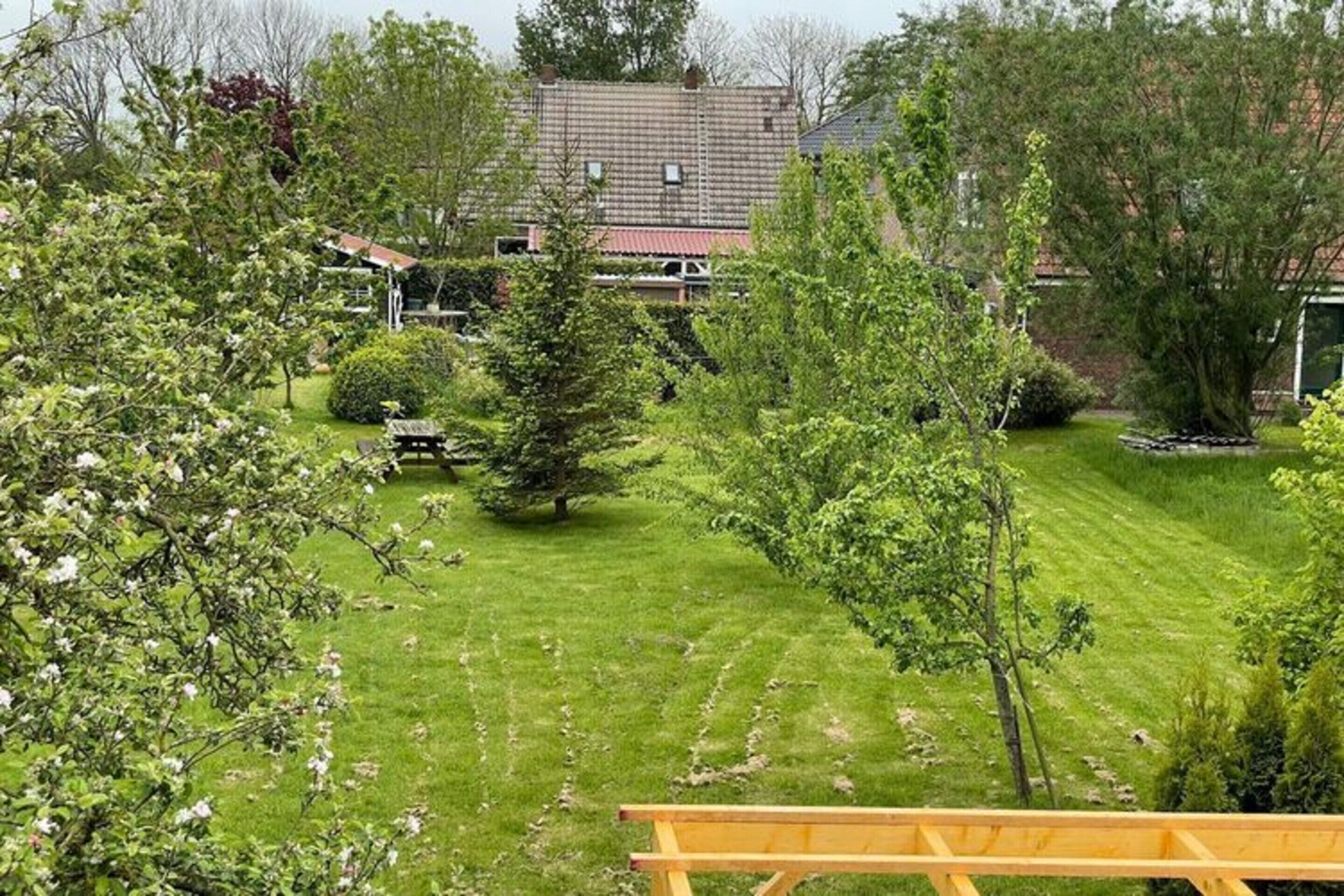 A well-maintained garden with a lawn, a wooden bench, and a house with a tiled roof in the background.